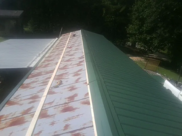 Old rusted panels beside newly installed green metal roofing — Wind Damage Roof Repair by Roofing Brothers in Frostproof