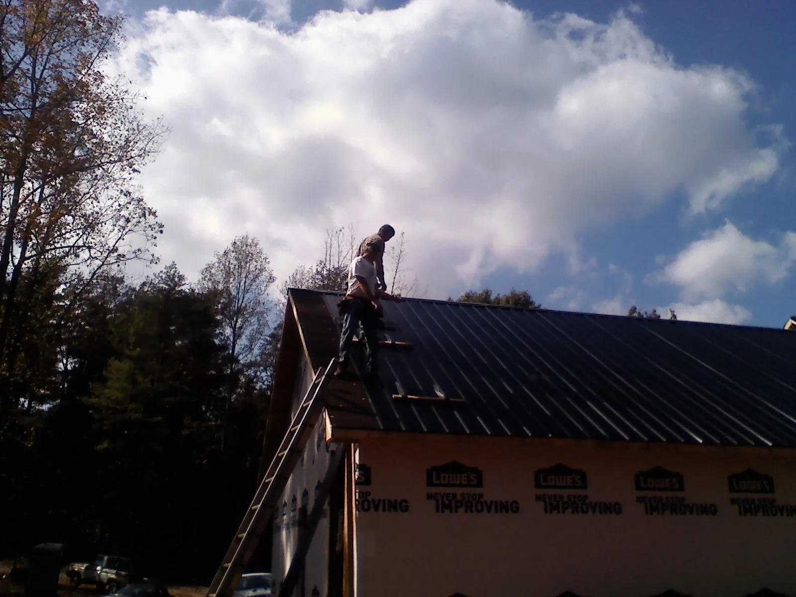 Roofer fastening dark metal panels high against a cloudy sky, from a Roof Inspection job in Frostproof